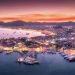 Aerial view of boats and beautiful city at night in Marmaris, Turkey. Amazing landscape with boats in marina bay, sea, city lights, mountains, red sky, clouds. Top view from drone.Harbor with yacht